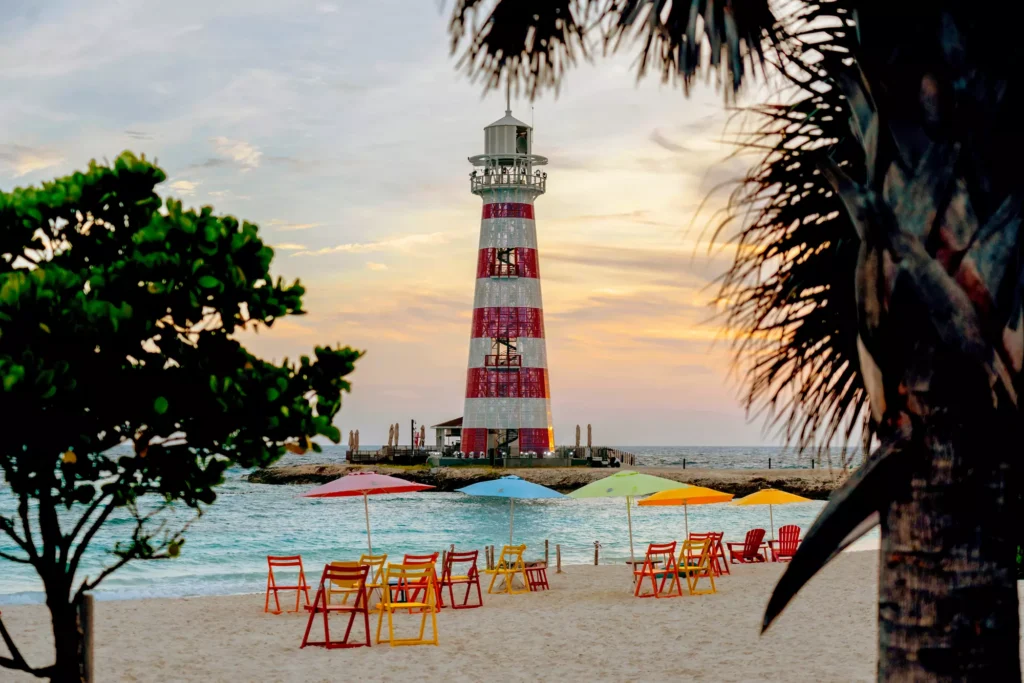 A serene beach scene at Ocean Cay MSC Marine Reserve featuring a lighthouse, palm trees, and sun loungers