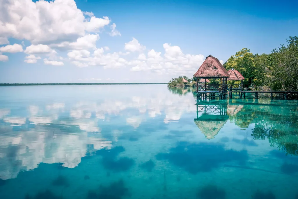 A serene view of Bacalar Lagoon with calm waters reflecting the sky and a charming overwater bungalow