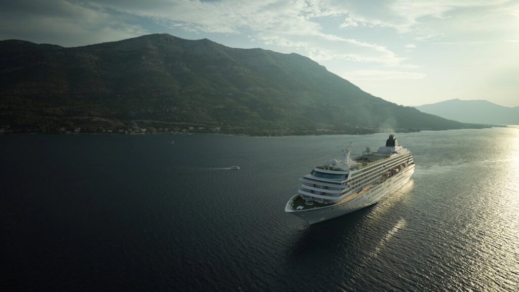 Crystal cruise ship cruising past green mountains in soft evening light