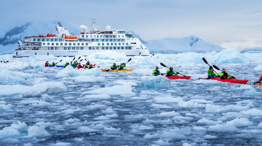 Kayakers paddling through sea ice near an expedition ship