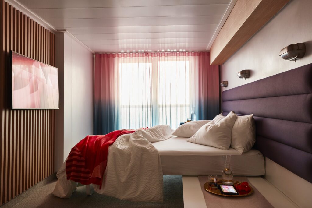 Sea Terrace cabin bed with red throw aboard Virgin Voyages
