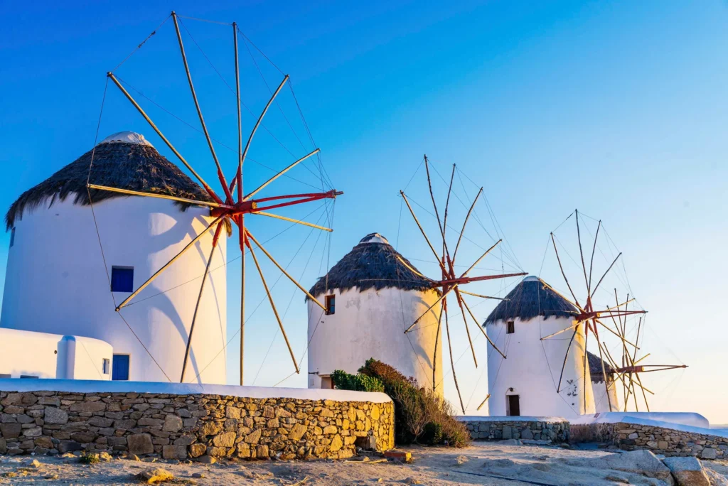 Three iconic windmills against a vibrant sky during sunset in Mykonos, Greece